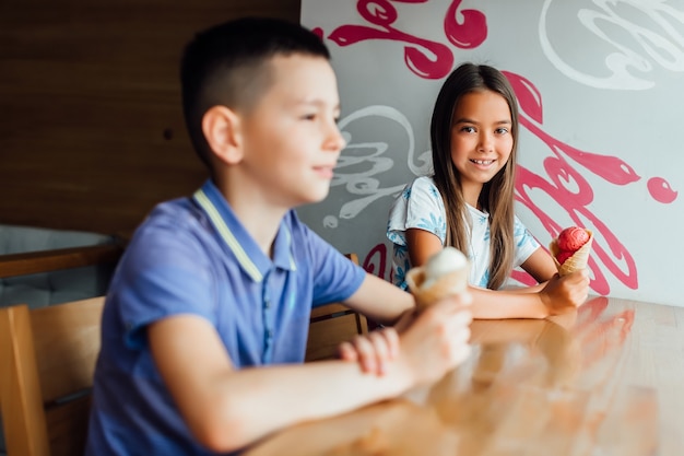 Niños felices relajándose con helado en las manos en la cafetería un día de verano juntos.