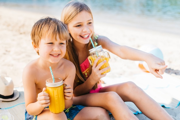 Niños felices sonriendo con bebida en la costa