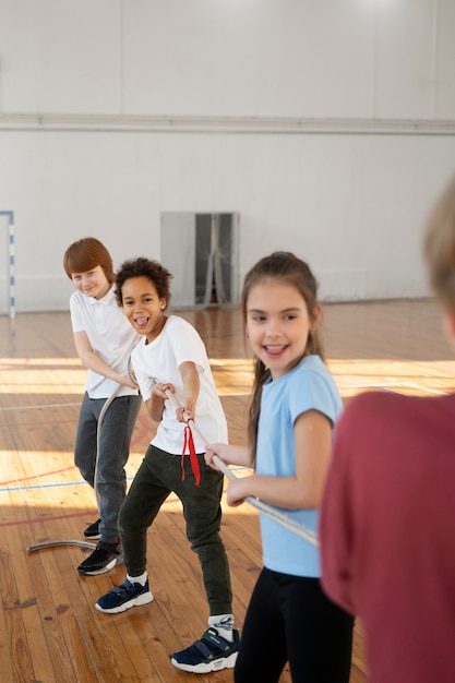 Niños fuertes sonrientes tirando de la cuerda en el gimnasio