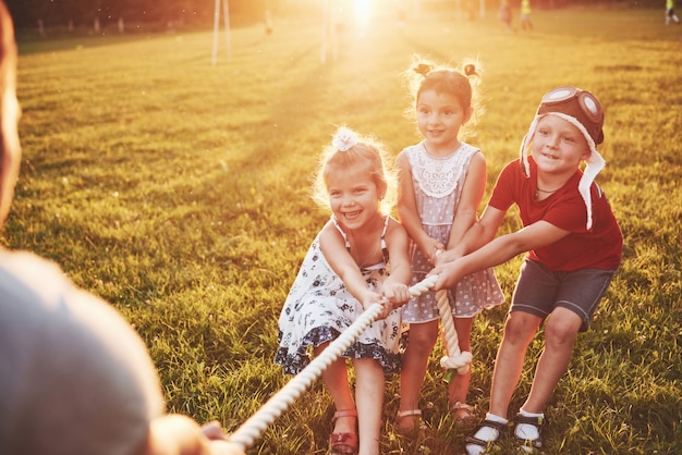 Los niños juegan con papá en el parque. Tiran de la cuerda y se divierten tendidos en un día soleado