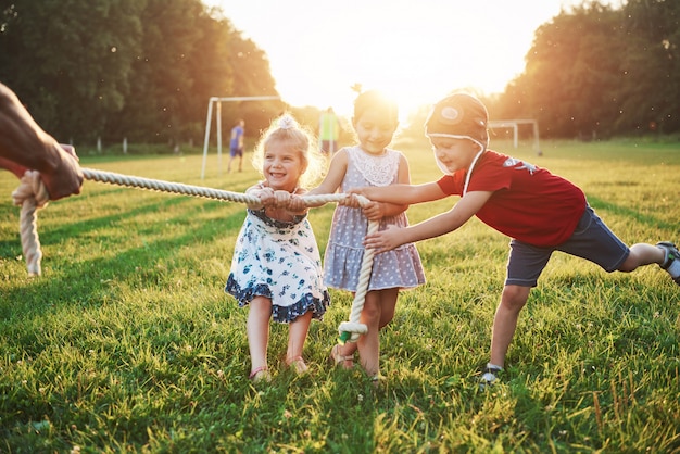 Los niños juegan con papá en el parque. Tiran de la cuerda y se divierten tendidos en un día soleado