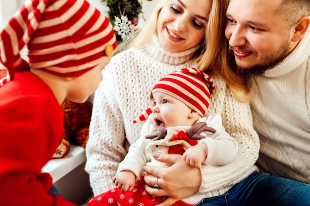 Los niños juegan sentados en las rodillas de los padres en una habitación decorada para la víspera de Navidad