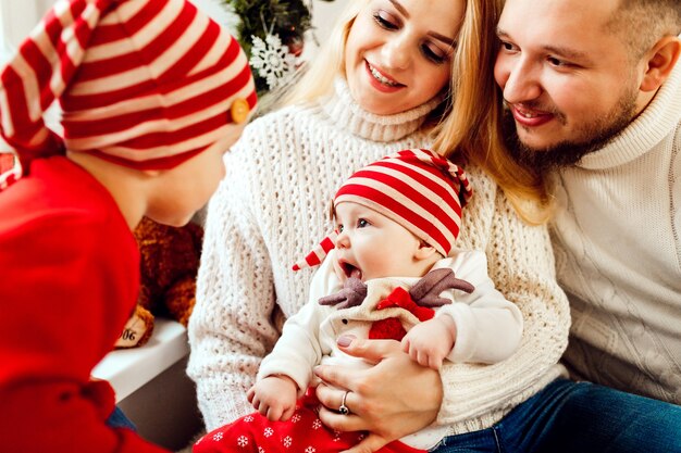 Los niños juegan sentados en las rodillas de los padres en una habitación decorada para la víspera de Navidad