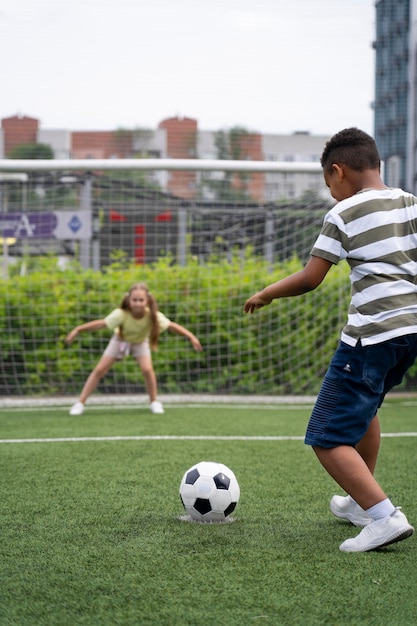 Foto gratuita niños jugando al fútbol en el campo de tiro completo