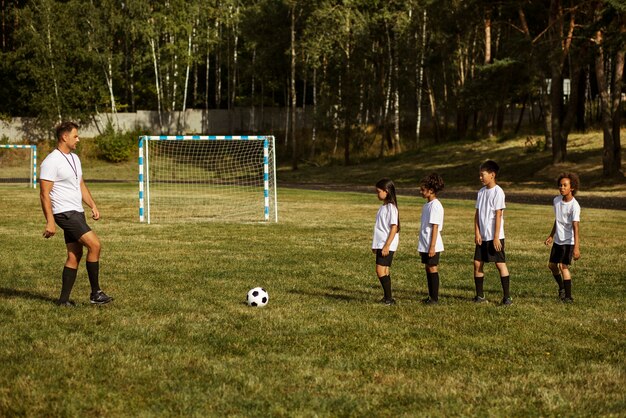 Niños jugando al fútbol supervisados por un entrenador de fútbol