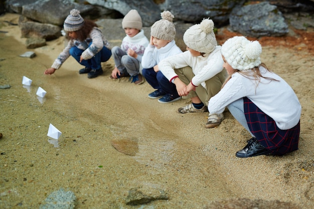 Foto gratuita niños jugando con barcos de papel en el lago