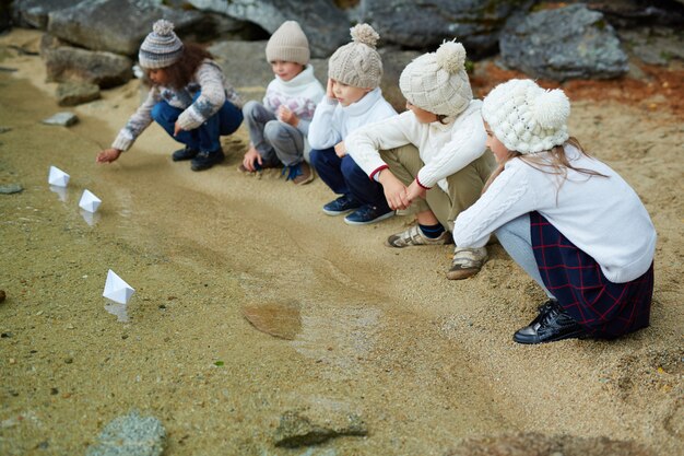 Niños jugando con barcos de papel en el lago