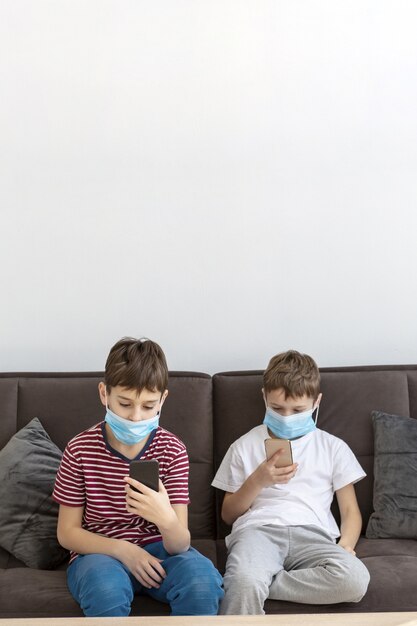Niños jugando en teléfonos inteligentes mientras usan máscaras médicas
