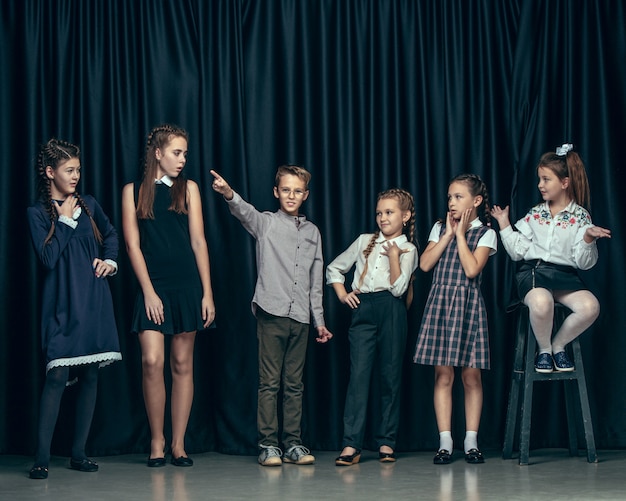 Niños lindos con estilo en estudio oscuro. Las hermosas chicas adolescentes y el niño de pie juntos