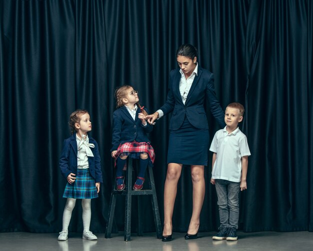 Niños lindos con estilo en estudio oscuro. Las hermosas chicas adolescentes y el niño de pie juntos