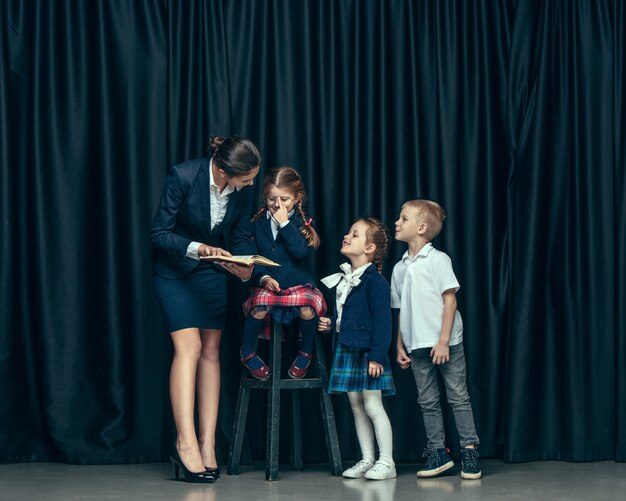 Niños lindos con estilo en estudio oscuro. Las hermosas chicas adolescentes y el niño de pie juntos