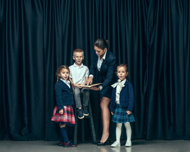 Niños lindos con estilo en estudio oscuro. Las hermosas chicas adolescentes y el niño de pie juntos