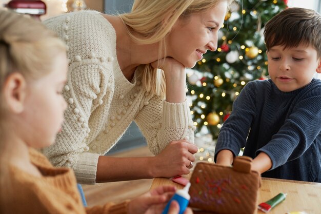 Los niños y la madre decorando la casa de pan de jengibre.