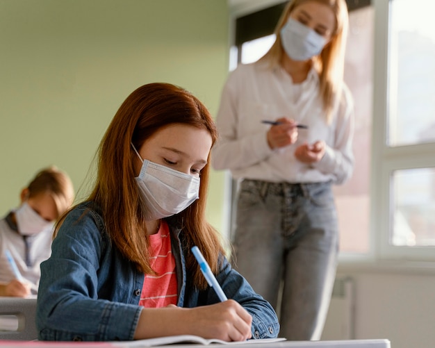 Niños con máscaras médicas aprendiendo en la escuela con maestra