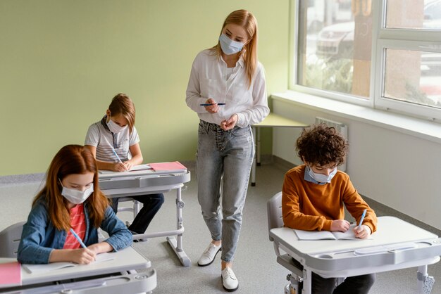 Niños con máscaras médicas aprendiendo en la escuela con el maestro.