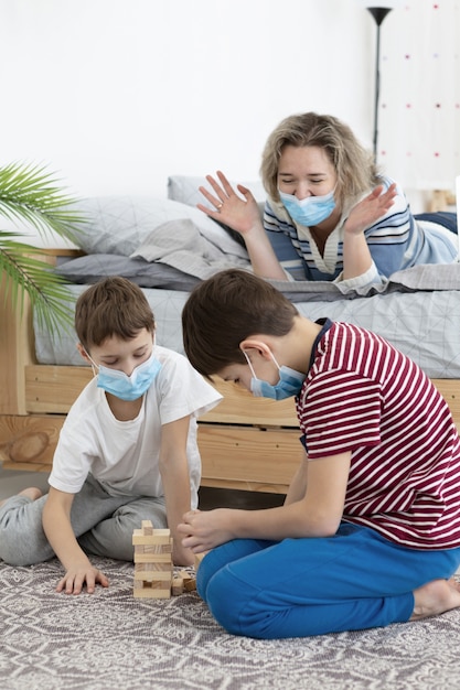 Niños con máscaras médicas jugando jenga en casa con madre