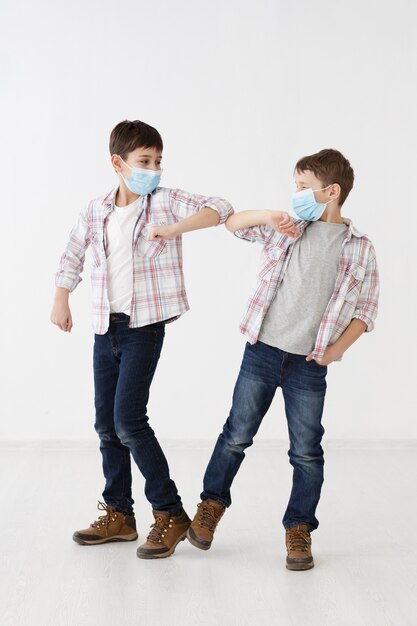 Niños con máscaras médicas que demuestran saludos sin contacto