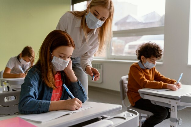 Niños con máscaras médicas que estudian en la escuela con el maestro.