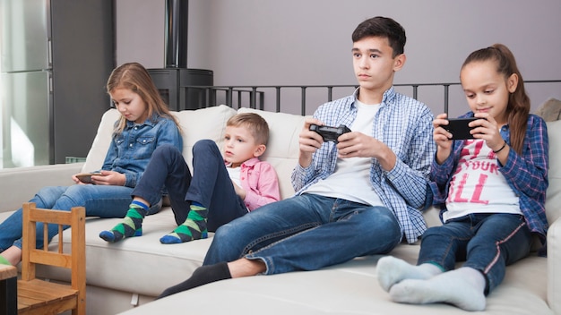 Foto gratuita niños navegando por teléfonos inteligentes cerca de adolescente con controlador