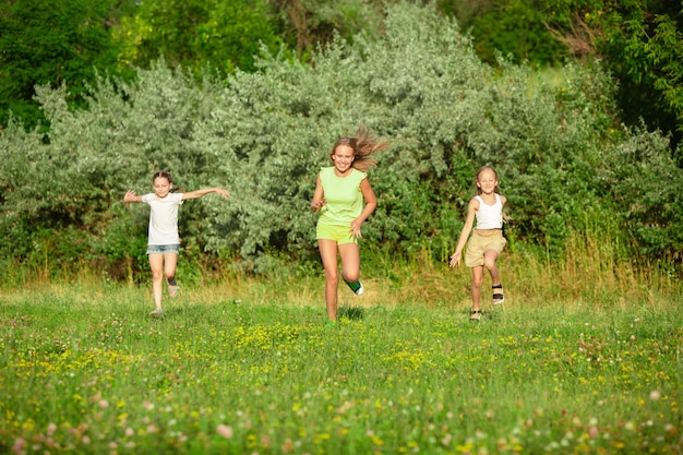 Niños, niños corriendo en la pradera en la luz del sol del verano