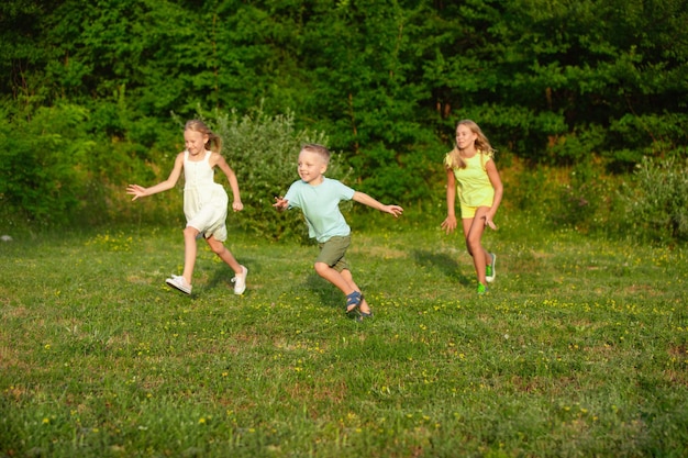 Niños, niños corriendo en la pradera en la luz del sol del verano