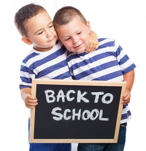 Niños pequeños abrazados con una pizarra negra con el mensaje "back to school"