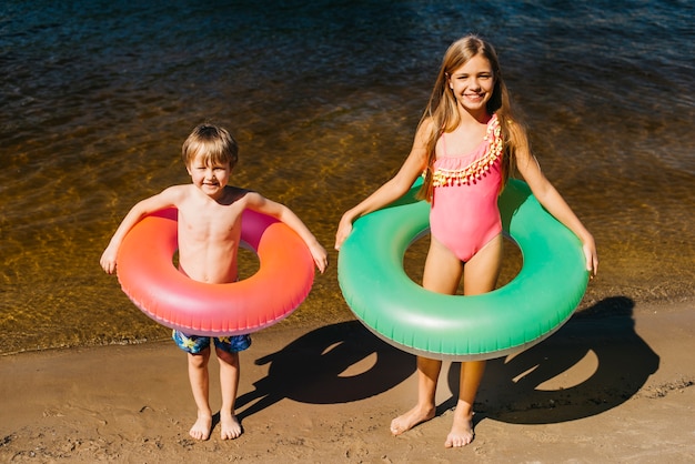 Foto gratuita niños pequeños con anillos de natación en la playa