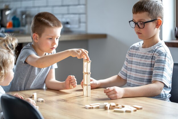 Los niños pequeños juegan un juego de mesa con cubos de madera en casa en la cocina.