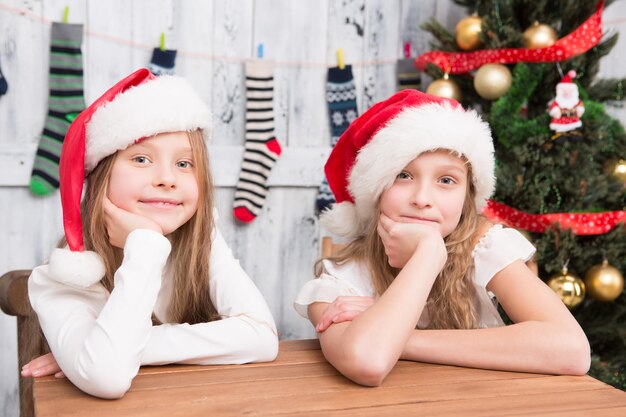 Niños pequeños sentados en la mesa y sonriendo a la cámara. Chicas guapas esperando la celebración de Año Nuevo y Navidad.