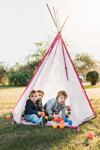 Niños pequeños sentados en tipi y jugando con pelotas