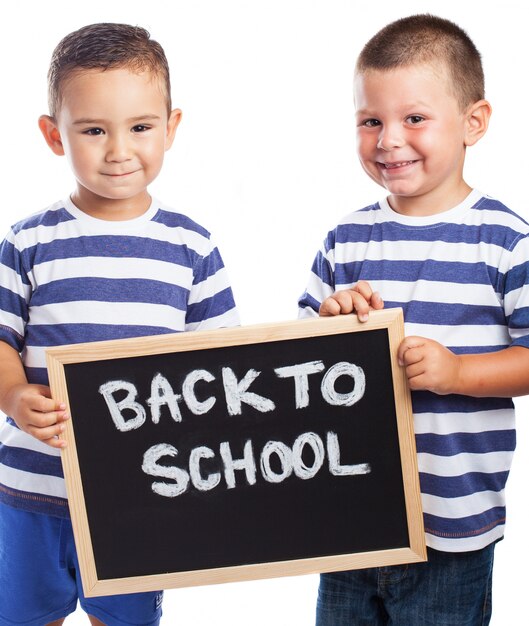Niños pequeños sonriendo con una pizarra negra con el mensaje "back to school" 