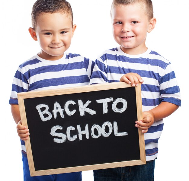 Niños pequeños sonriendo con una pizarra negra con el mensaje "back to school" 