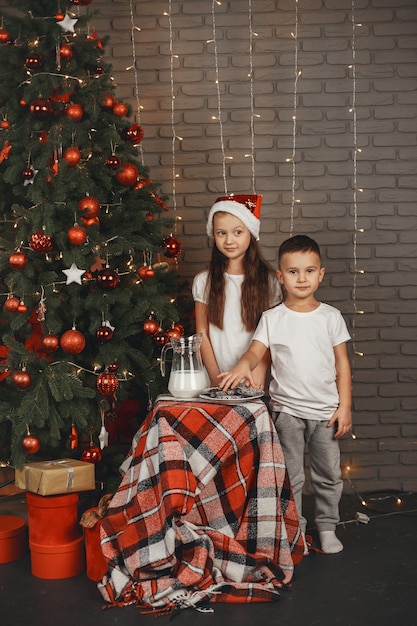 Foto gratuita niños de pie cerca del árbol de navidad. niños comiendo galletas con leche.