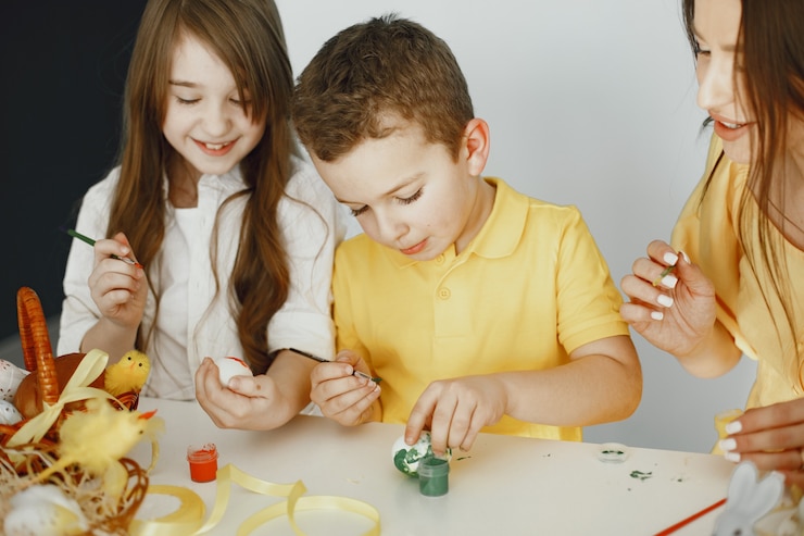 Foto gratuito los niños pintan huevos. la madre enseña a los niños. sentado en una mesa blanca.