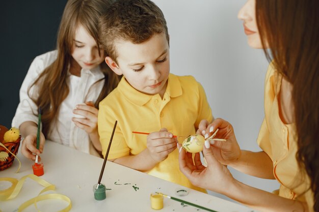 Los niños pintan huevos. La madre enseña a los niños. Sentado en una mesa blanca.