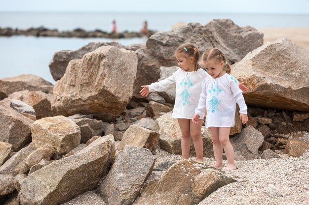 Niños en la playa del mar. Gemelos de pie contra piedras y agua de mar.