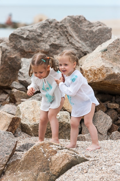 Niños en la playa del mar. Gemelos de pie contra piedras y agua de mar.