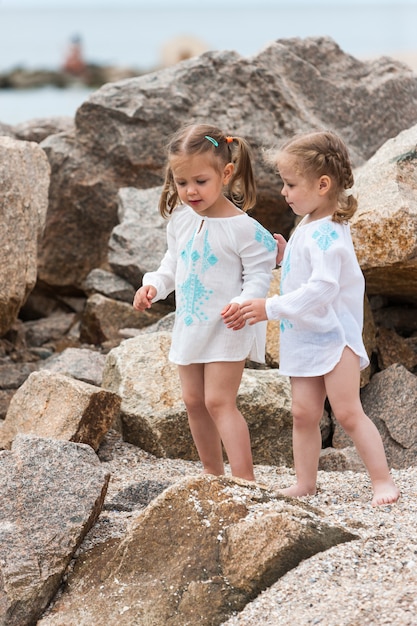 Niños en la playa del mar. Gemelos de pie contra piedras y agua de mar.