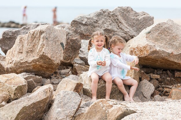 Niños en la playa del mar. Gemelos sentados contra piedras y agua de mar.