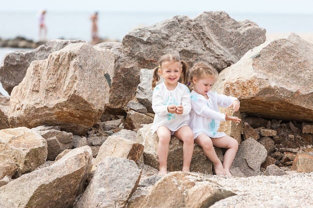 Niños en la playa del mar. Gemelos sentados contra piedras y agua de mar.