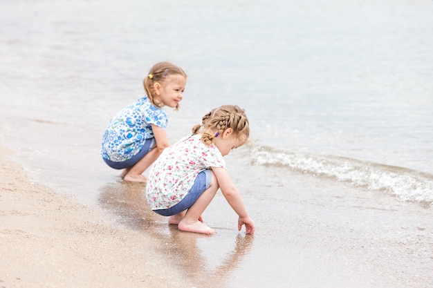 Niños en la playa del mar. Gemelos sentados junto al agua de mar.