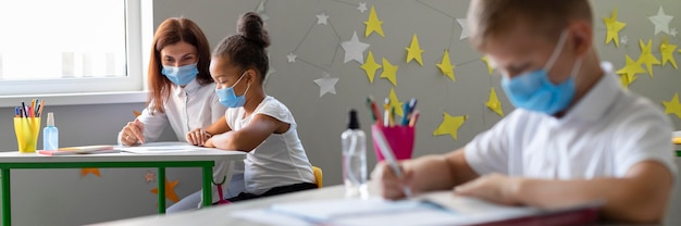 Niños y profesores con máscaras médicas en el aula.