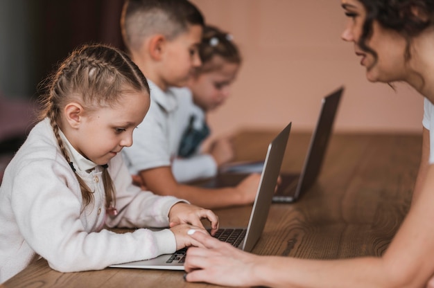 Los niños que usan computadoras portátiles en la escuela son ayudados por el maestro