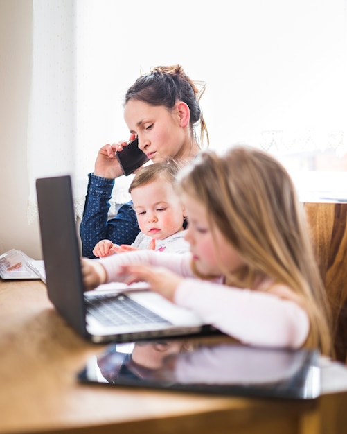 Niños sentados al lado de su madre hablando por teléfono móvil