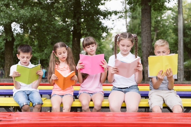 Foto gratuita niños sentados en el banco y leyendo.