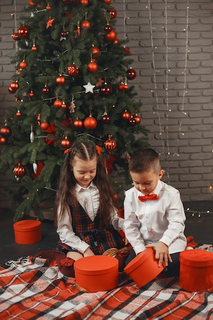 Niños sentados cerca del árbol de Navidad. Los niños abren cajas con regalos.