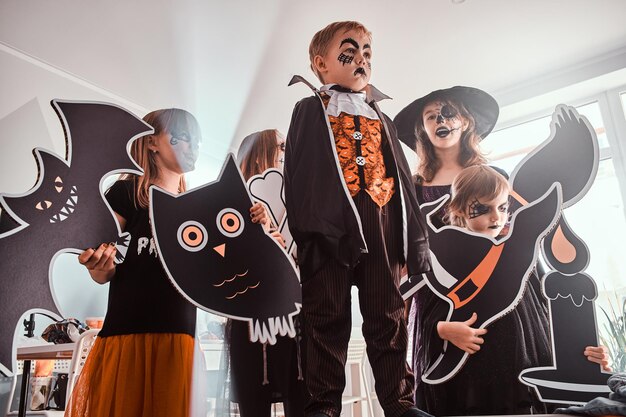 Niños serios con disfraces de Halloween posan para el fotógrafo mientras sostienen decoraciones.