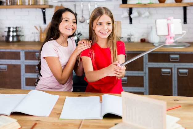 Niños sonrientes sentados en el escritorio y tomando autofotos en la cocina