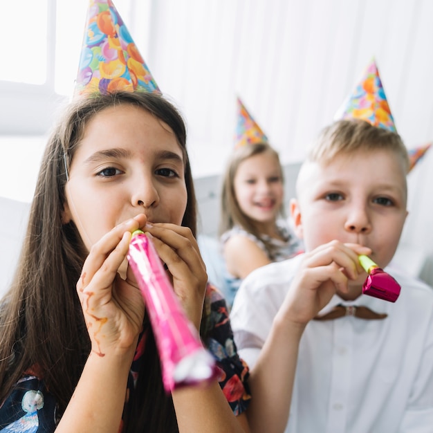 Niños soplando cuernos de fiesta a la cámara