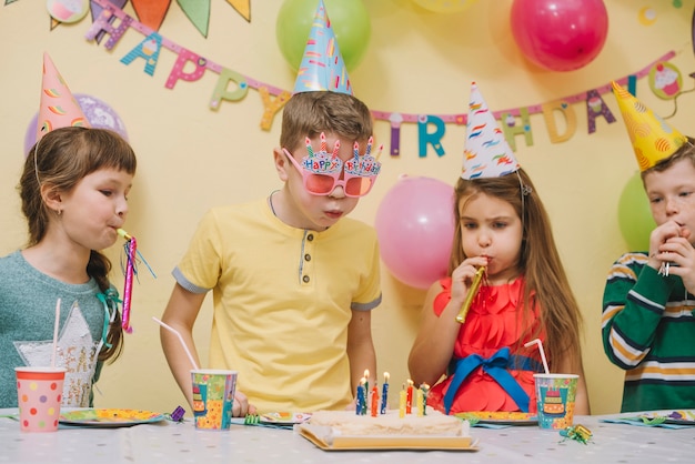 Niños soplando cuernos y velas en el pastel